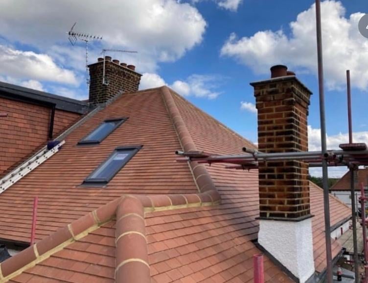 Residential roof under renovation with terracotta tiles, brick chimneys, and metal scaffolding against blue sky
