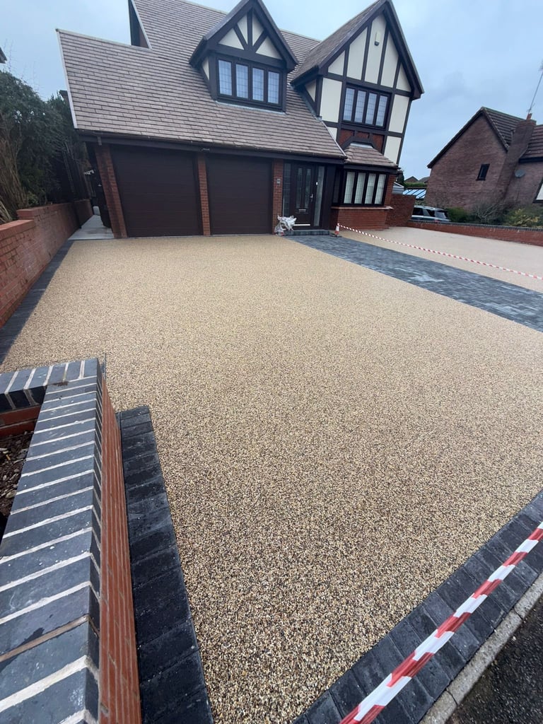 Modern Tudor-style house with large gravel driveway, dark garage doors, and brick boundary walls under clear sky