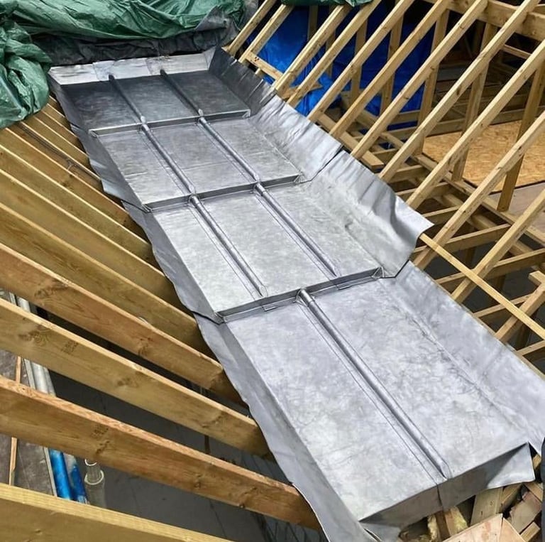 Metal roof panels being installed on wooden roof framing with rafters and blue underlayment visible during construction