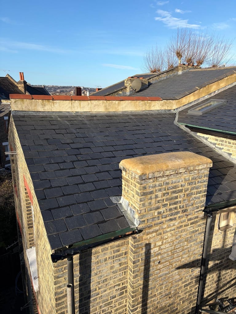Flat roof with dark slate tiles, brick chimney, and stone parapet walls on residential building