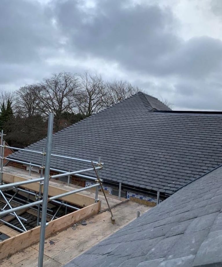 New gray slate roof installation on a residential building with metal scaffolding and bare trees visible against a cloudy sky