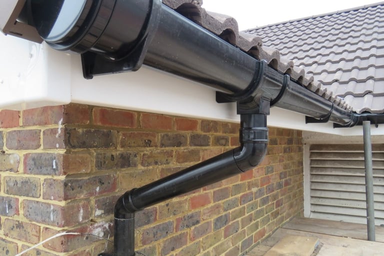 Black plastic guttering and downpipe installed on a brick house with grey tile roof