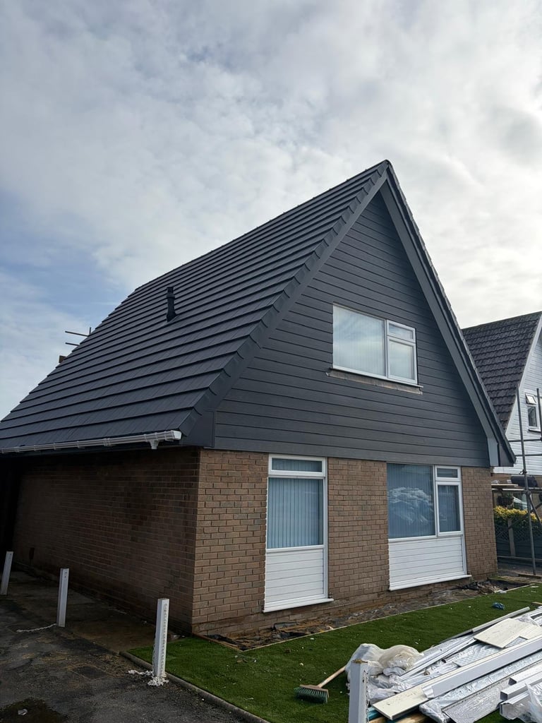 Modern residential home with dark pitched roof, brick and siding exterior, gable window, and attached garage under renovation