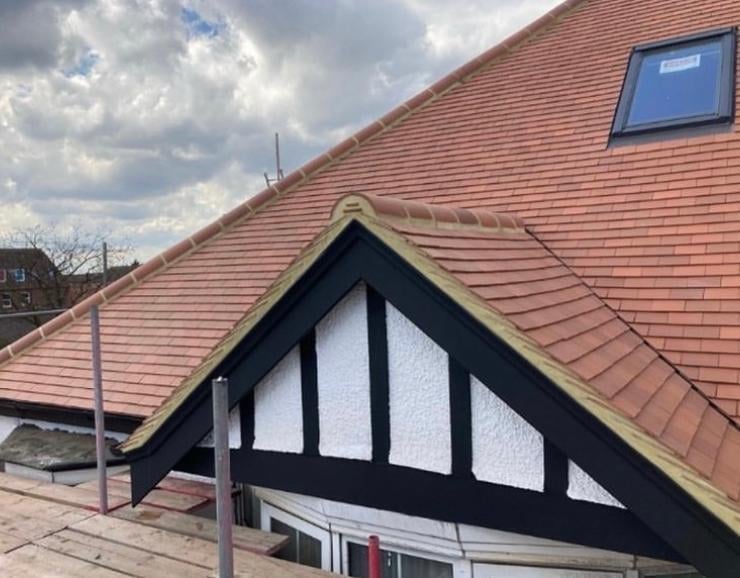 Steep pitched roof with terracotta tiles and Tudor-style black and white gable end featuring decorative half-timbering