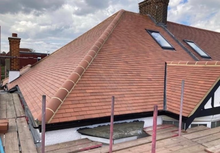 Red clay tile roof with dormers and chimneys under construction, supported by temporary pink metal scaffolding poles