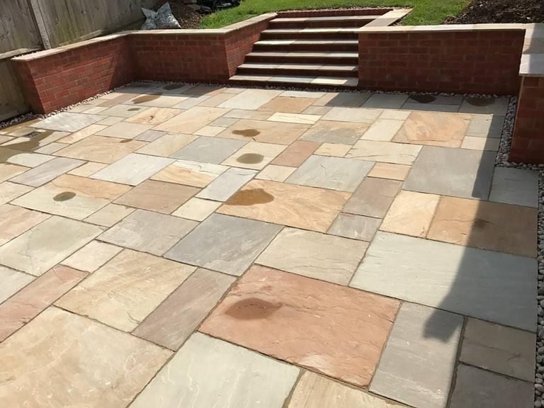 Paved patio with mixed terracotta and stone tiles, red brick retaining walls, and stairs leading to an upper level
