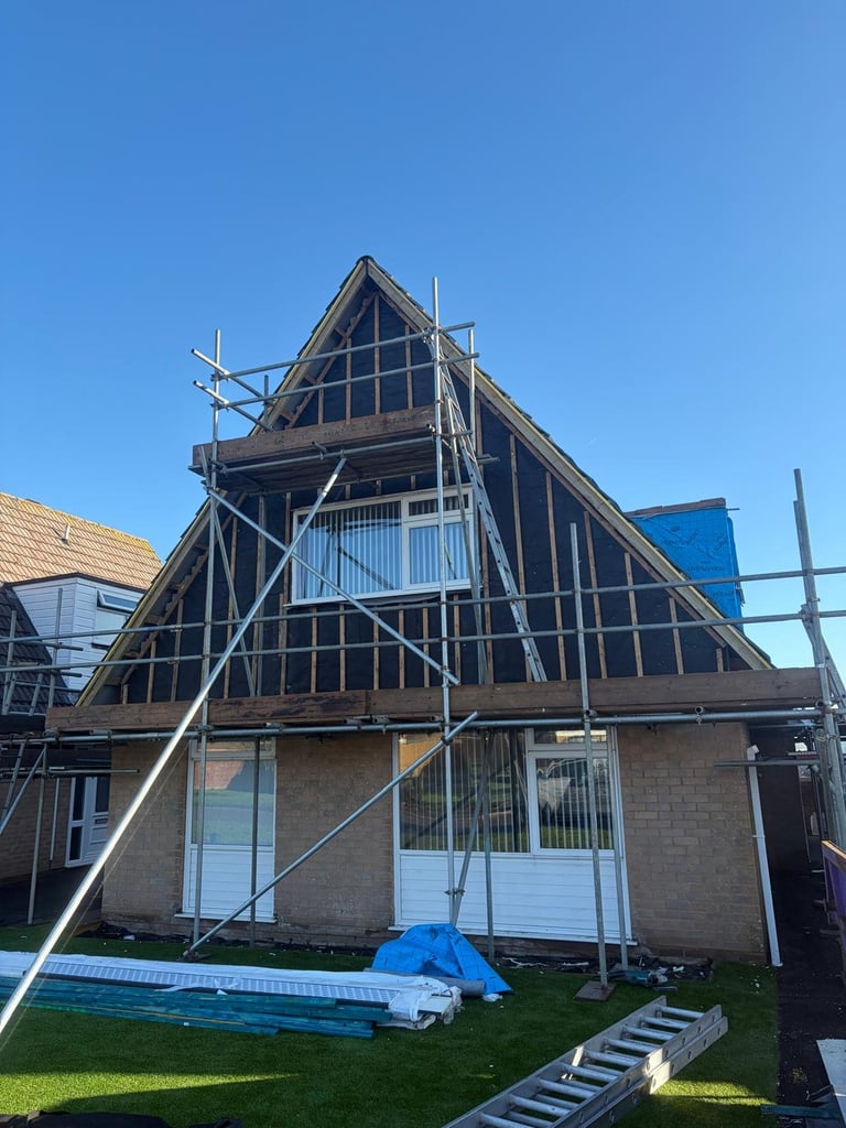 Traditional timber-framed Dutch house with steep gabled roof under renovation with metal scaffolding, set against clear blue sky