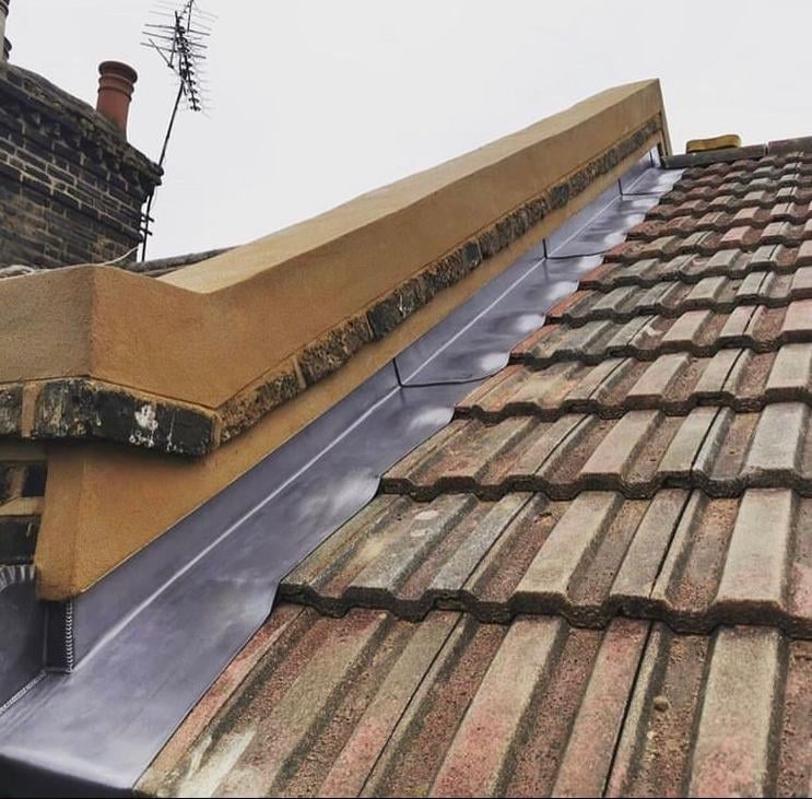 Roof with blue waterproof membrane installed along ridge and yellow metal flashing over terracotta tiles