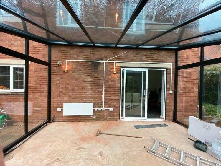 Interior of a brick enclosed patio with glass roof panels, glass doors, and pendant lights during construction