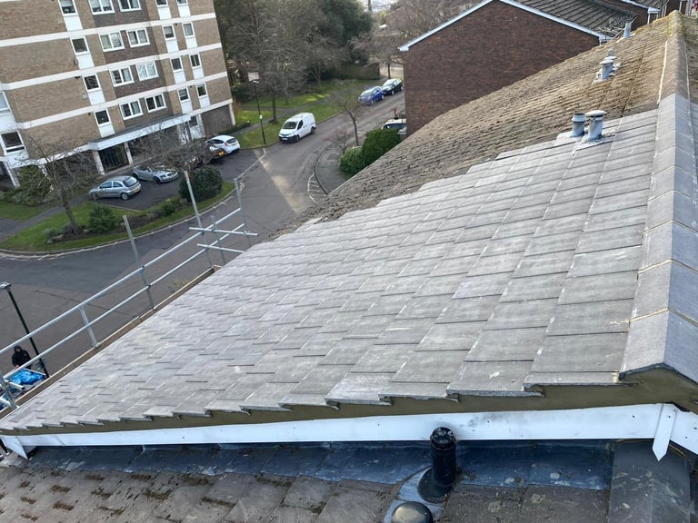 Aerial view of a tiled roof with white gutter and residential buildings and parked cars below