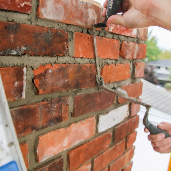 Person applying mortar between red bricks with a trowel during masonry work on a brick wall