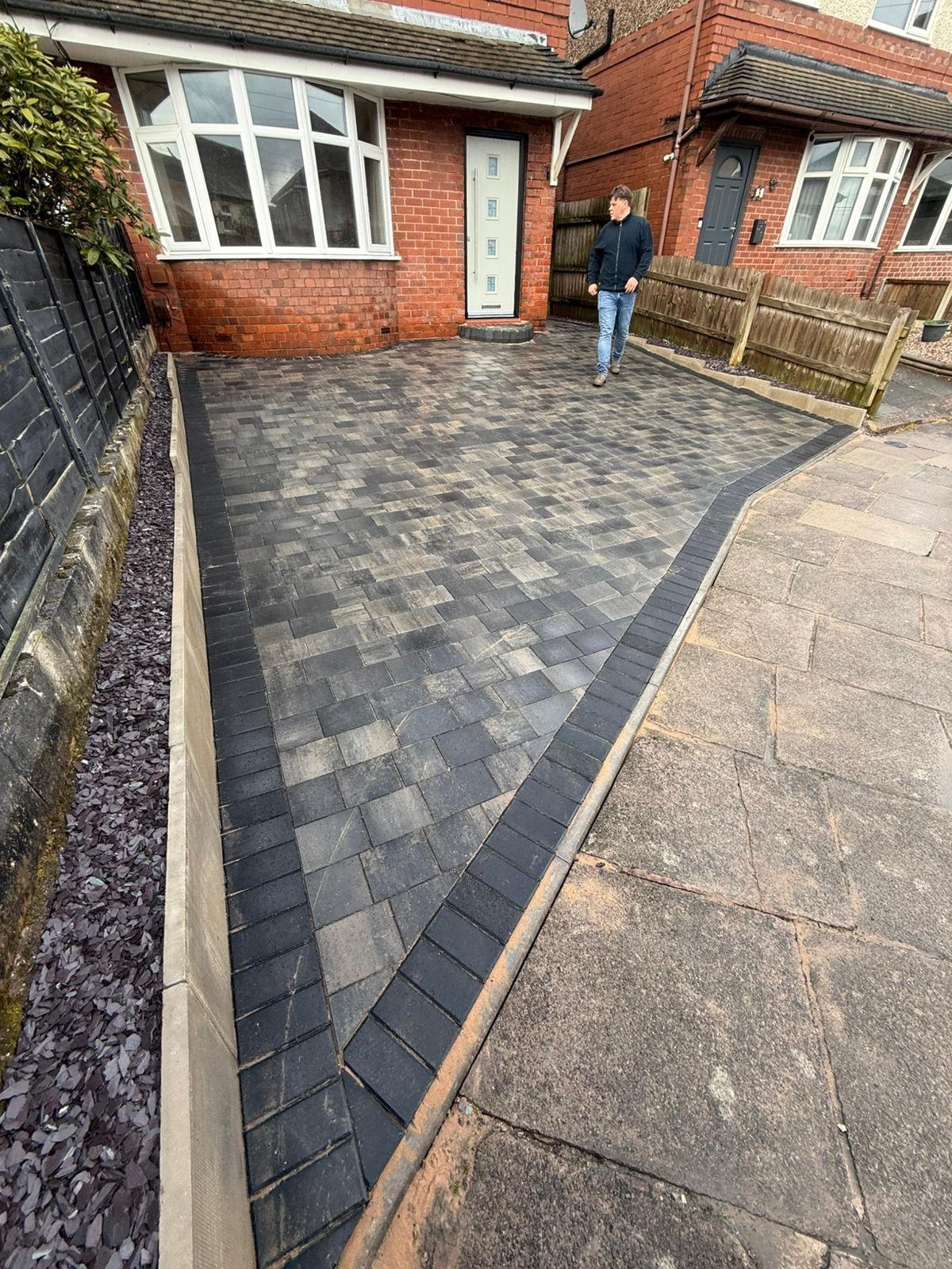 Newly installed dark patterned brick driveway outside a red brick residential home with person standing in background