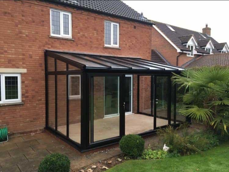 Modern black-framed glass conservatory attached to a brick home with manicured garden