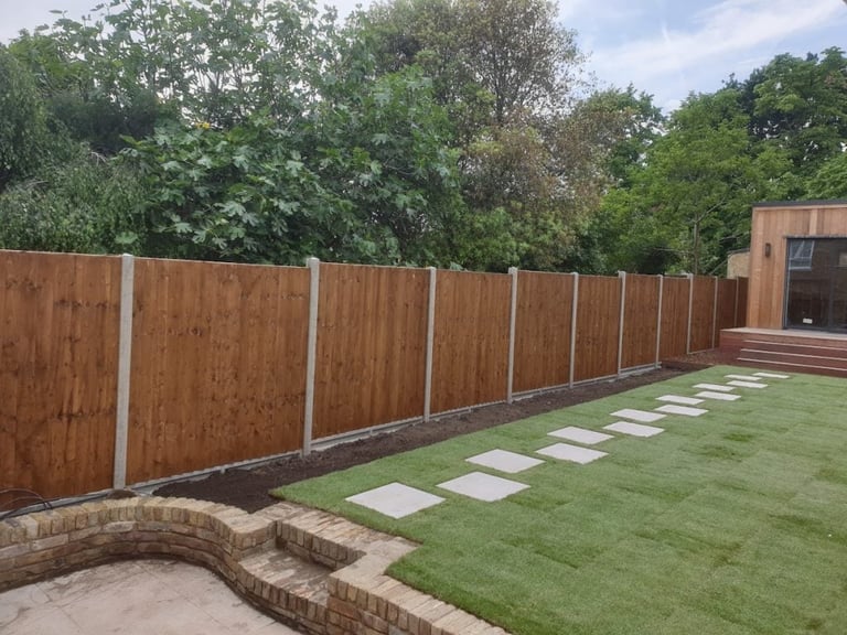 Backyard garden with wooden fence, stepping stone path, brick edging, and mature green trees in background