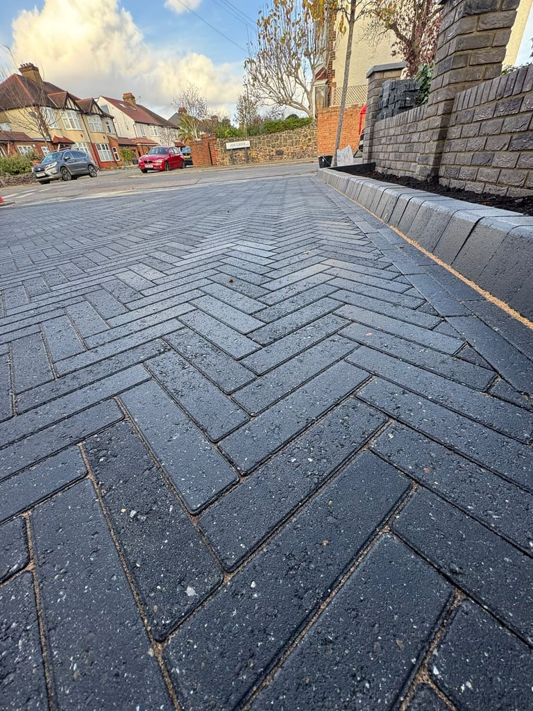 Herringbone patterned driveway with slate-colored pavers in front of brick buildings and parked cars