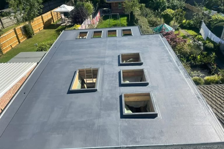 Aerial view of a modern flat roof with three rectangular skylights and surrounding residential properties