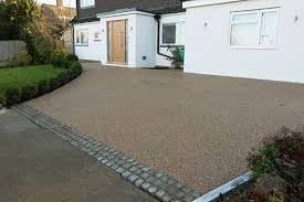 Modern house with large gravel driveway bordered by stone edging, featuring a white exterior and manicured landscaping