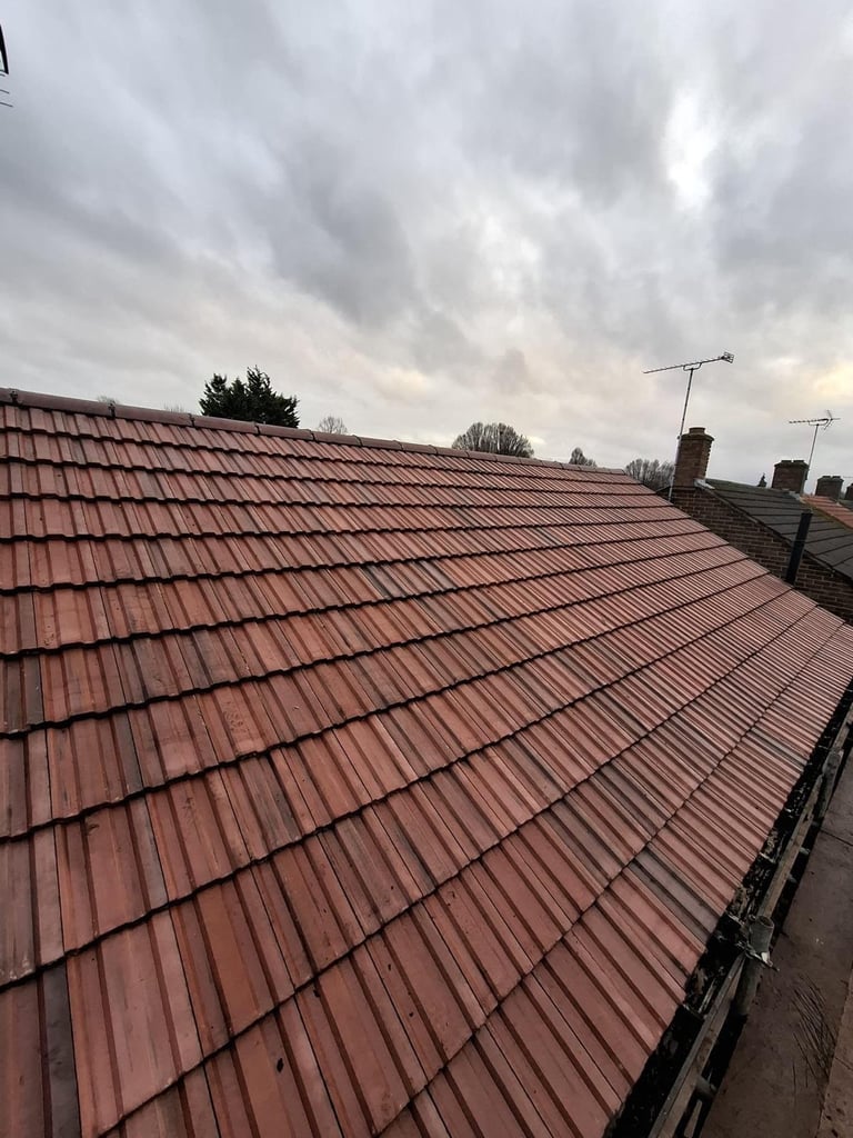 Aerial view of a terracotta tiled roof with chimneys and TV antennas against a cloudy sky
