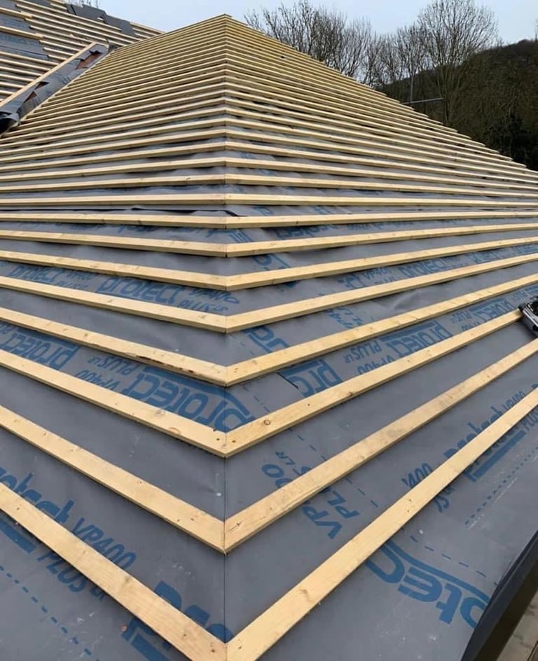 Roof construction showing wooden rafters with blue underlayment and insulation layers during building work