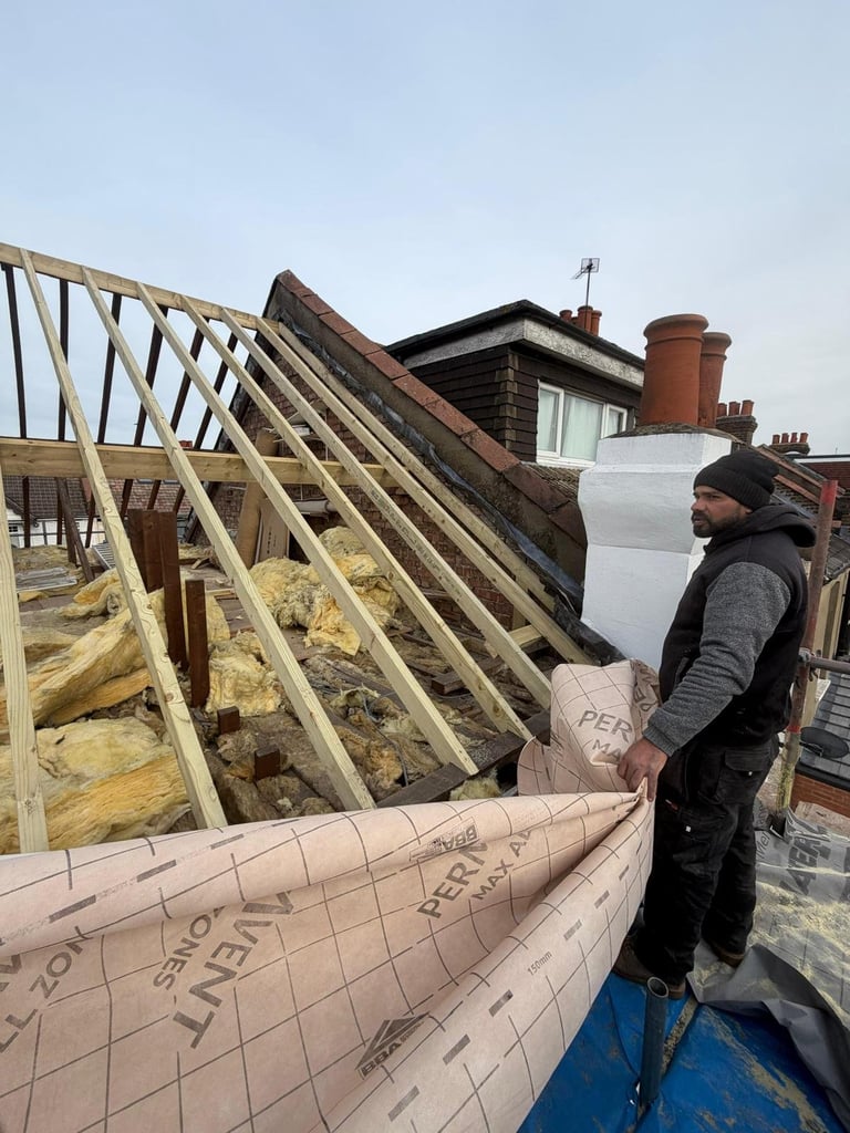 Construction worker on rooftop with exposed roof frame, insulation, and building materials during roof renovation