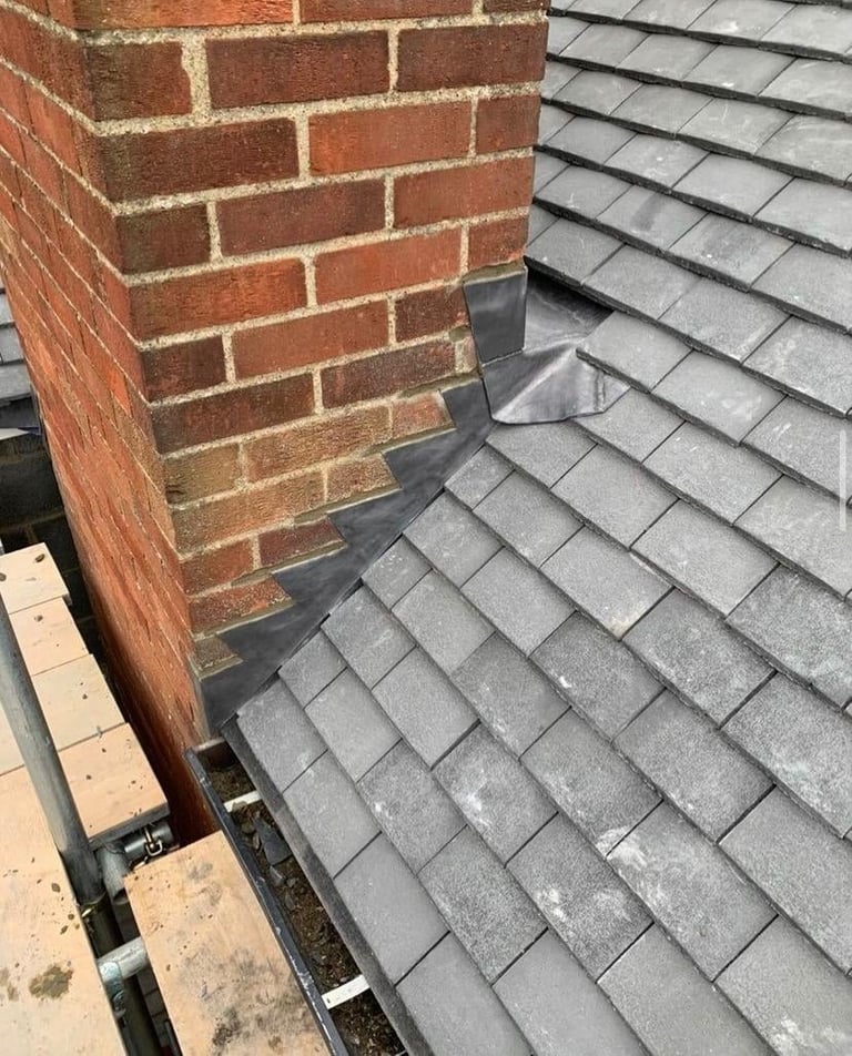 Red brick chimney extending over gray tiled roof with metal flashing at the junction