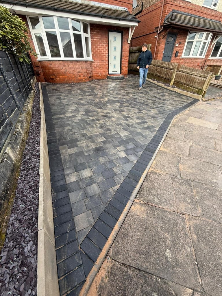 Newly paved driveway with charcoal patterned pavers in front of a brick residential home with white windows and door